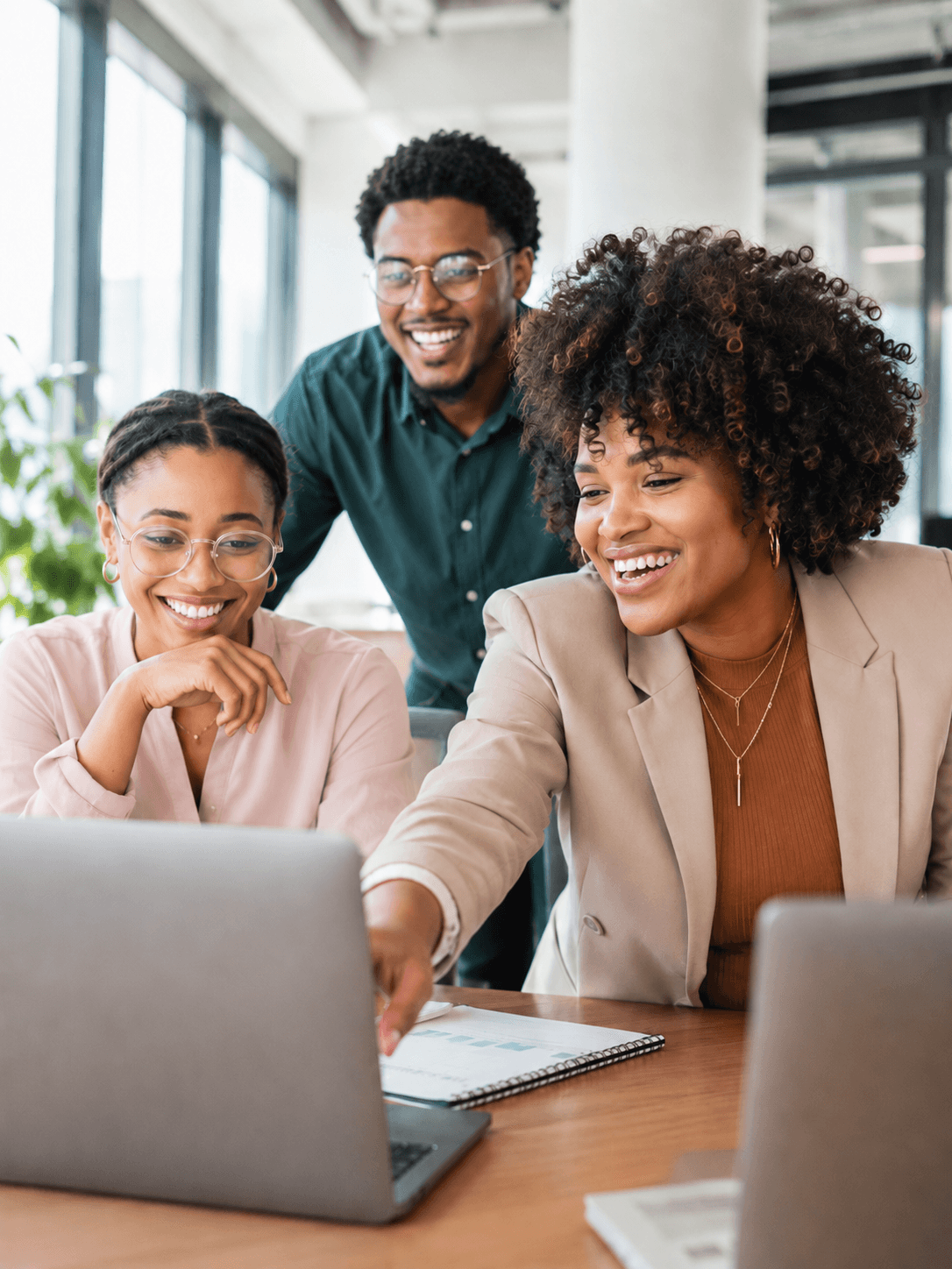 Trois personnes souriantes regardent l’écran d’un ordinateur portable autour d’une table de bureau ; l’une d’elles désigne l’écran.