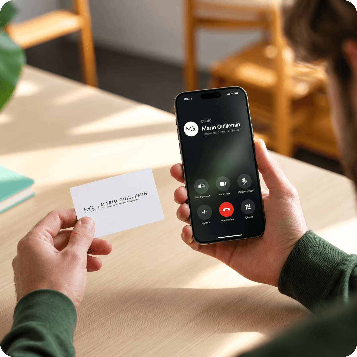 Une personne tient une carte de visite et un smartphone affichant un appel de Mario Guillemin, Consultant & Product Builder.